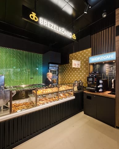 Innenansicht des Brezelkönig Shop & Café mit Brezelauslage, Kaffeezone und grün gefliester Wand.