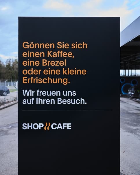 Schwarze Werbetafel vor dem Shop & Café mit Hinweis auf Kaffee, Brezeln und Erfrischungen.