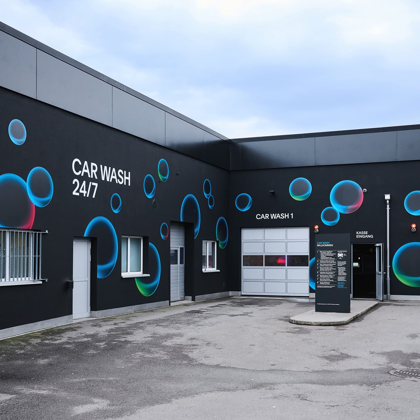 Aussenansicht der Car Wash 24/7 bei The Yards in Rümlang mit schwarzer Fassade, blauen Kreismotiven und Einfahrt zur Waschanlage.