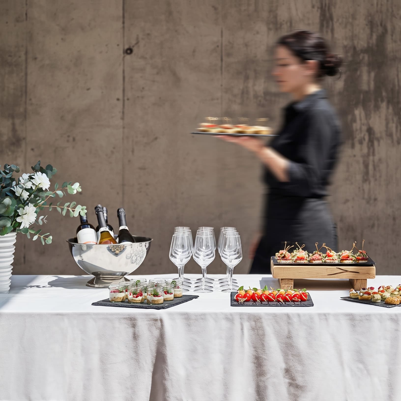 Serviceperson trägt Apérohäppchen an einem Buffet mit Fingerfood, Wein und Gläsern bei The Yards Events.