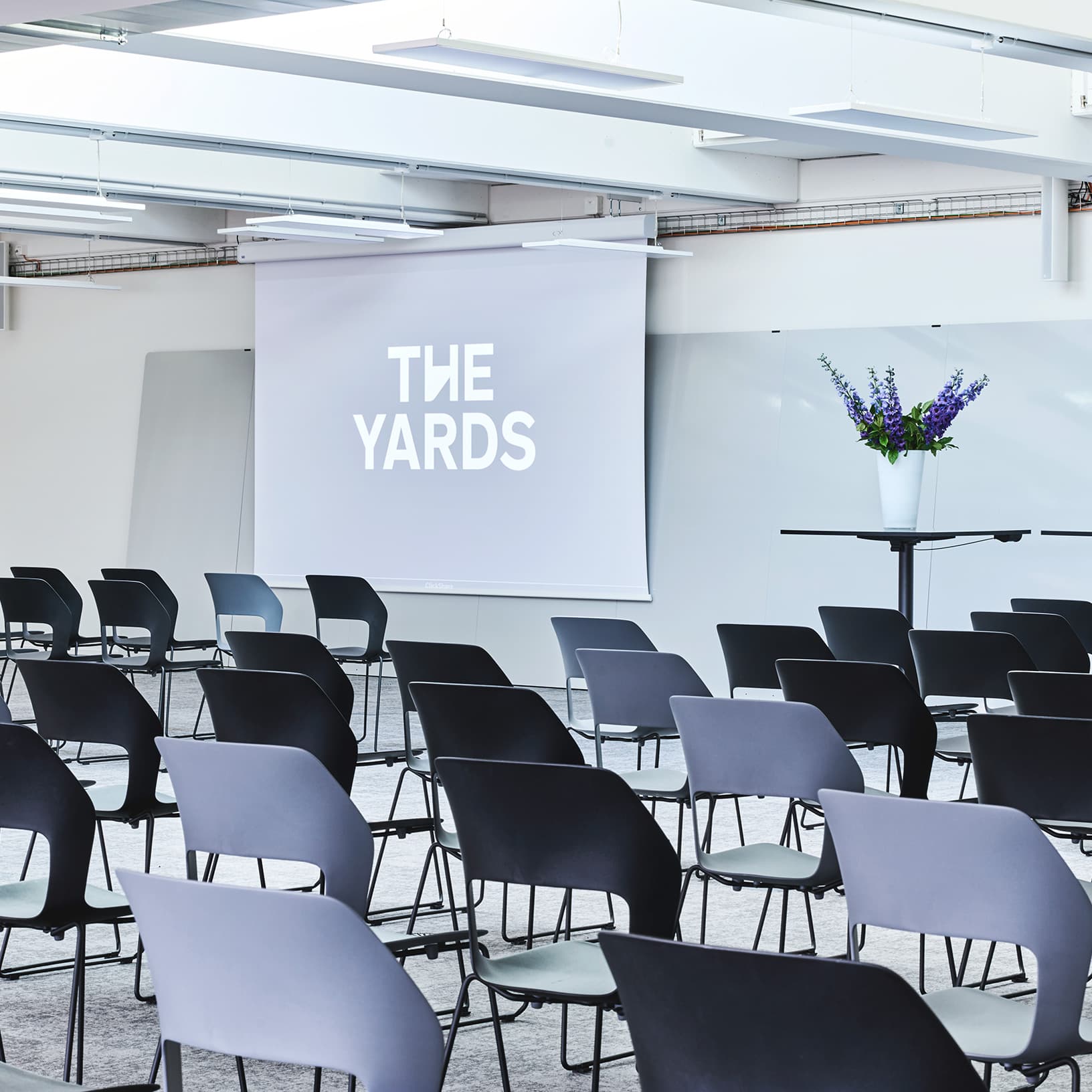 Konferenzbestuhlung mit Leinwand und Präsentationsbereich im lichtdurchfluteten Saal von The Yards Events.