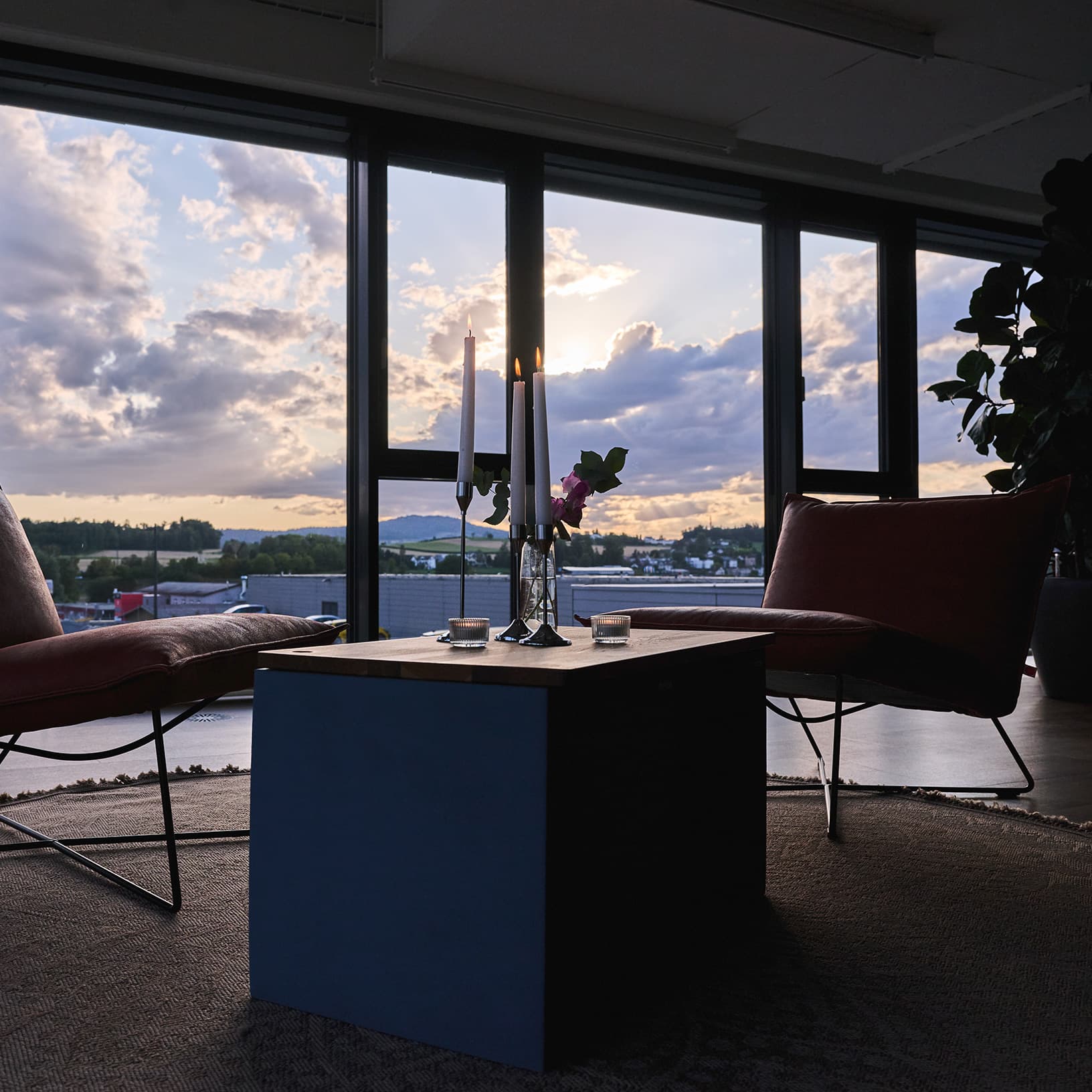 Lounge mit Sesseln, Kerzenlicht und Panoramafenstern bei Sonnenuntergang in The Yards Events.