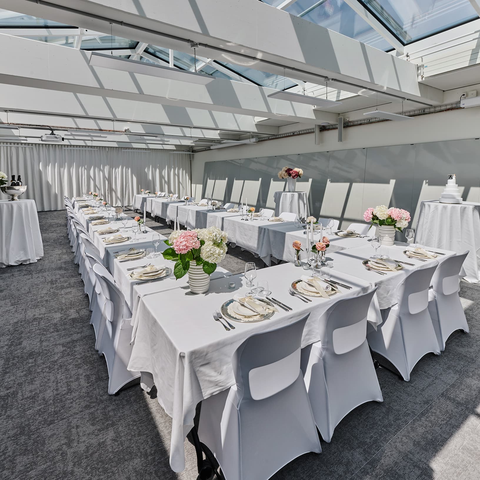 Festlich gedeckte Tafeln mit Blumenschmuck und Kerzen in der lichtdurchfluteten Eventlocation von The Yards Events.