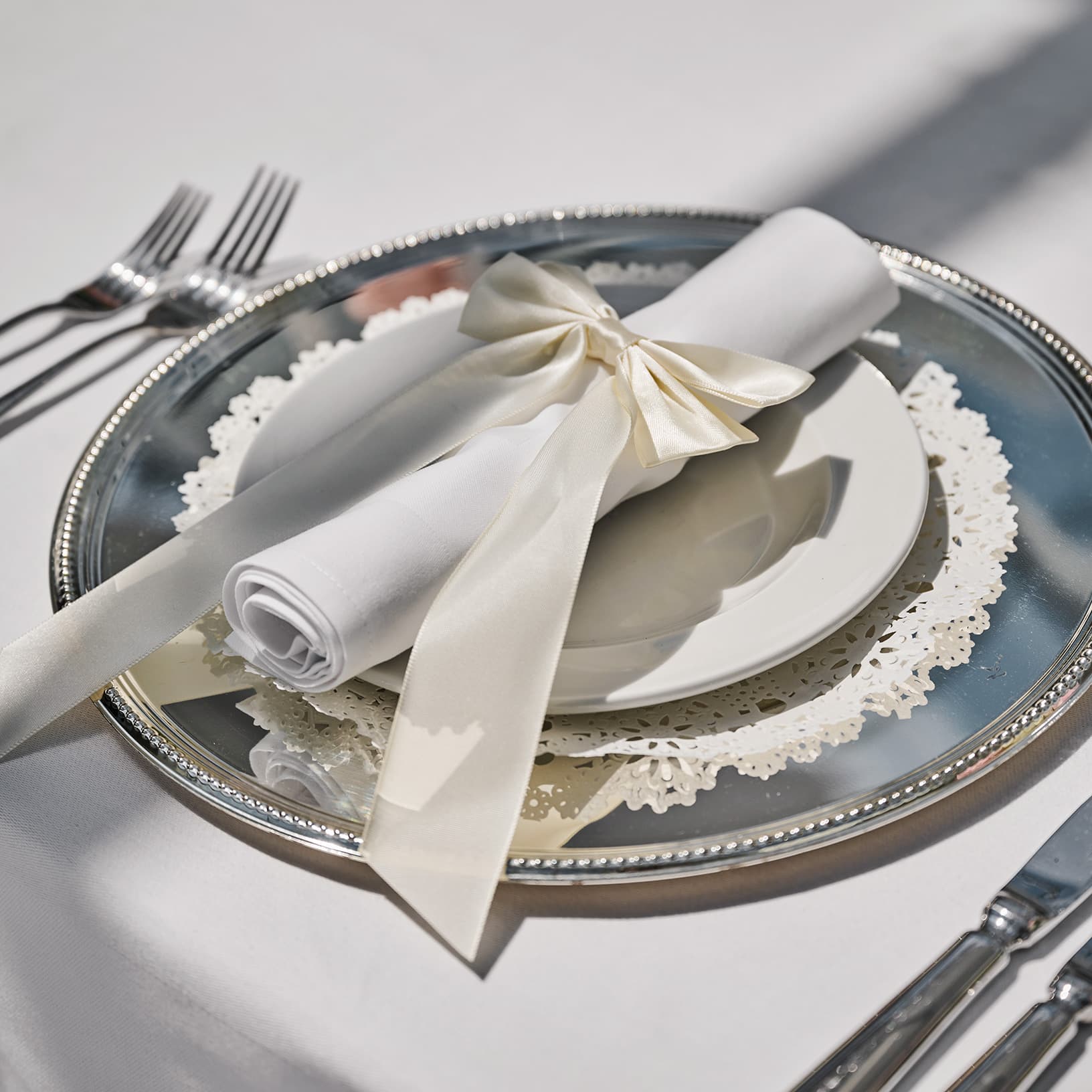 Festliches Tischgedeck mit silbernem Platzteller und weisser, mit Schleife gebundener Serviette.