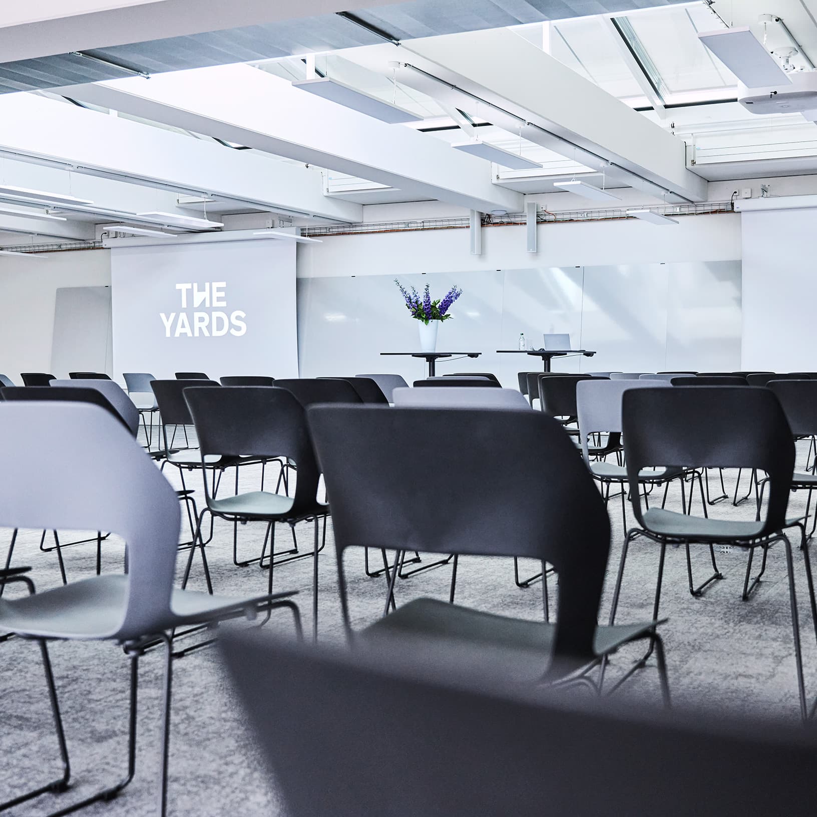Blick auf die Konferenzbestuhlung und den Präsentationsbereich mit Leinwand bei The Yards Events.