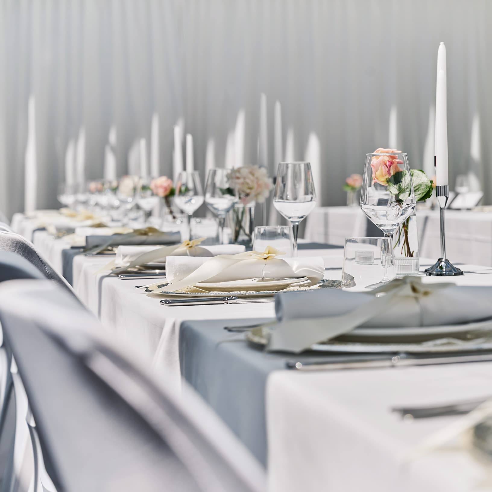 Festlich gedeckte Tafel mit weissen Tischdecken, Kerzen, Blumenschmuck und Gläsern bei The Yards Events.