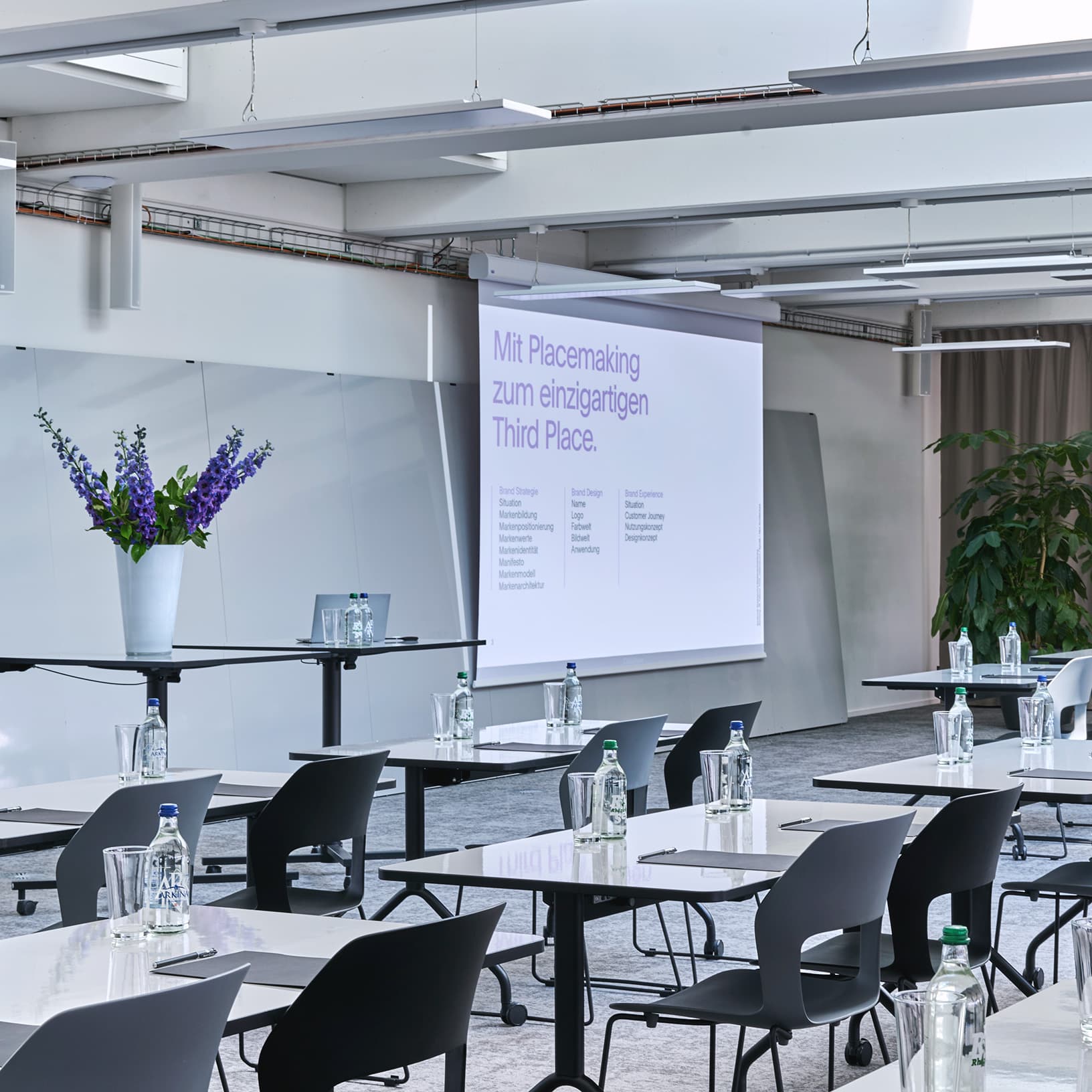 Seminarsetting mit Tischen, Stühlen und Präsentationsleinwand in The Yards Events.