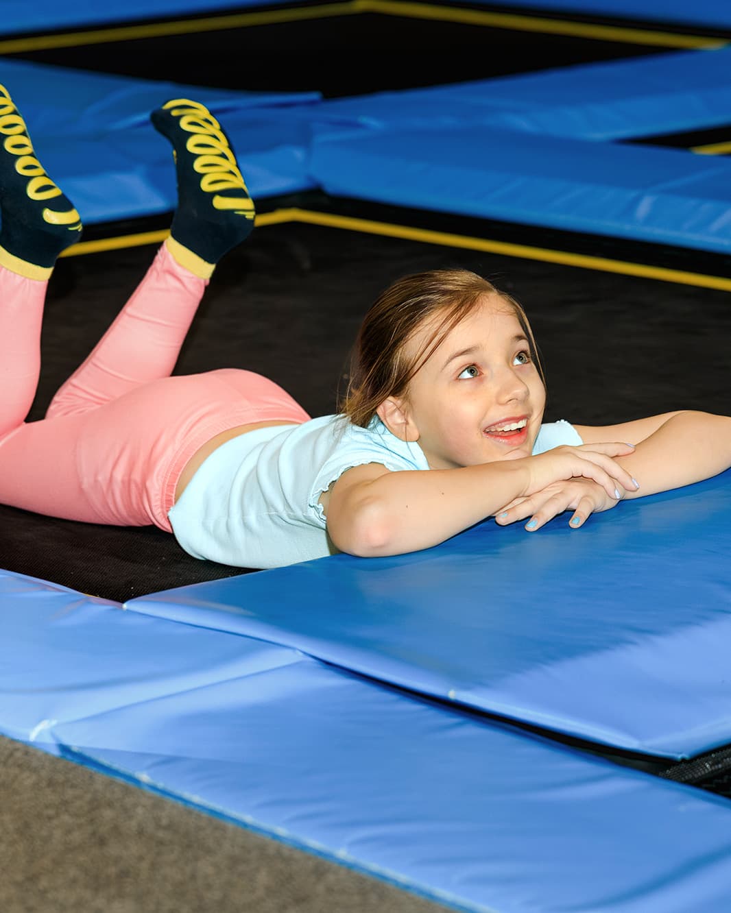 Lachendes Mädchen liegt auf einem Trampolin mit blauen Polstern im Flip Lab bei The Yards.