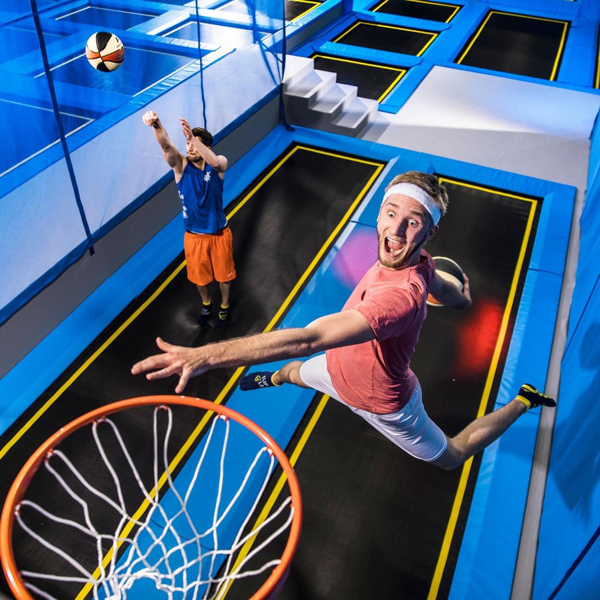 Zwei Personen springen in einer Trampolinhalle mit Basketballkorb im Flip Lab bei The Yards.