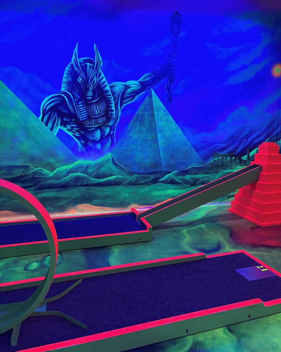Schwarzlicht-Minigolfbahnen vor einer ägyptischen Fantasiekulisse mit Pyramiden und grosser Figur bei Galaxy Golf.