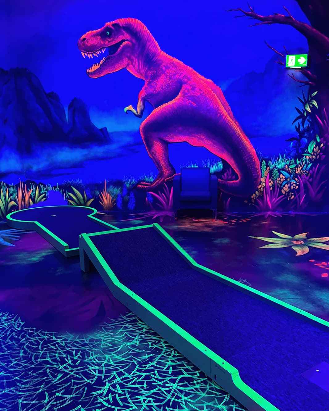 Neonbeleuchtete Minigolfbahn vor einem grossen Dinosaurier-Wandmotiv bei Galaxy Golf in The Yards.