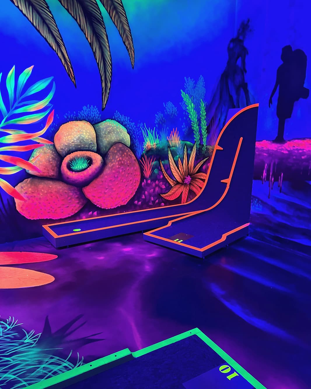Schwarzlicht-Minigolfbahn mit leuchtenden Fantasiepflanzen und geschwungener Rampe bei Galaxy Golf in The Yards.