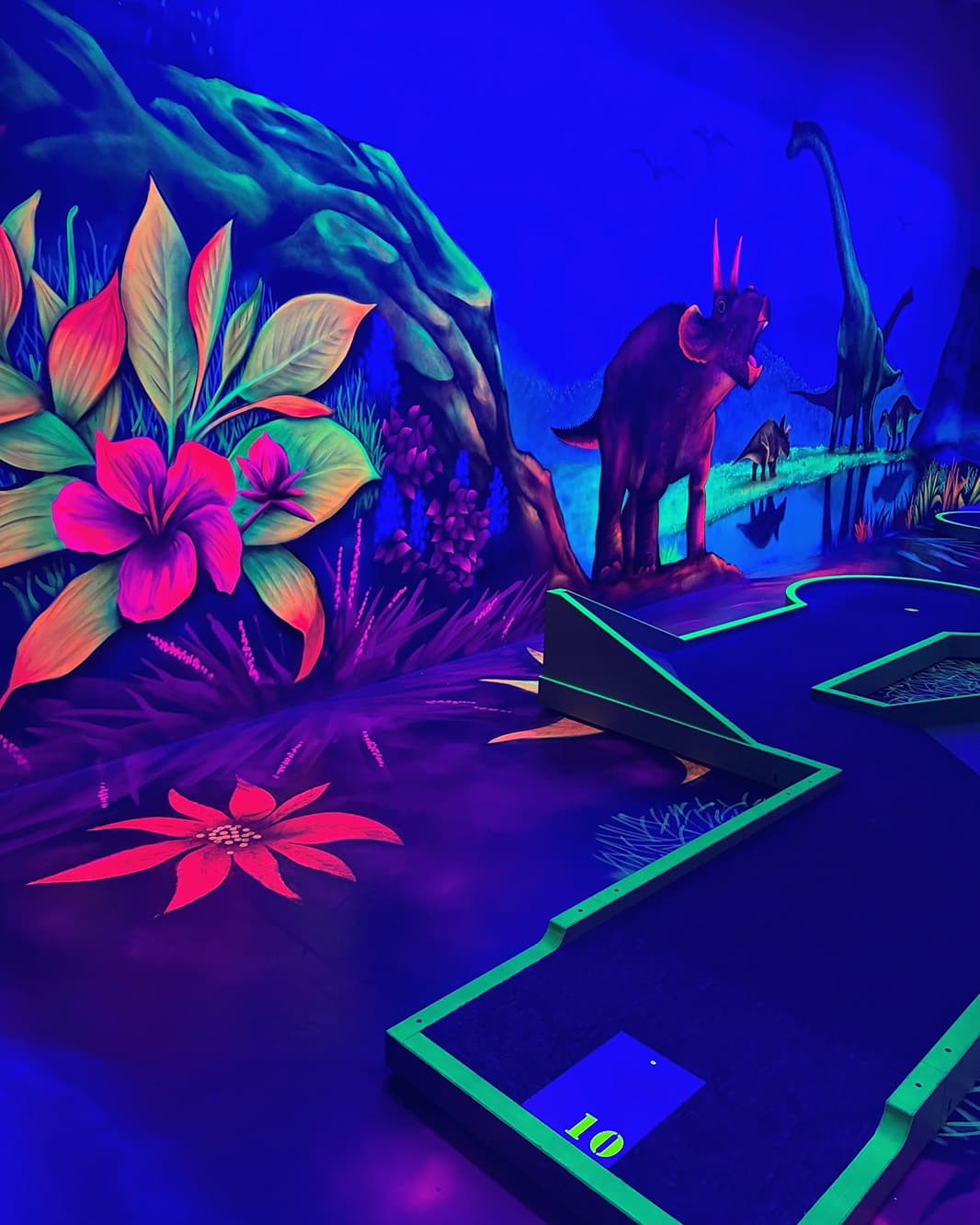 Minigolfbahn mit Dinosauriern und fluoreszierenden Pflanzen in einer farbigen Urzeitkulisse bei Galaxy Golf.