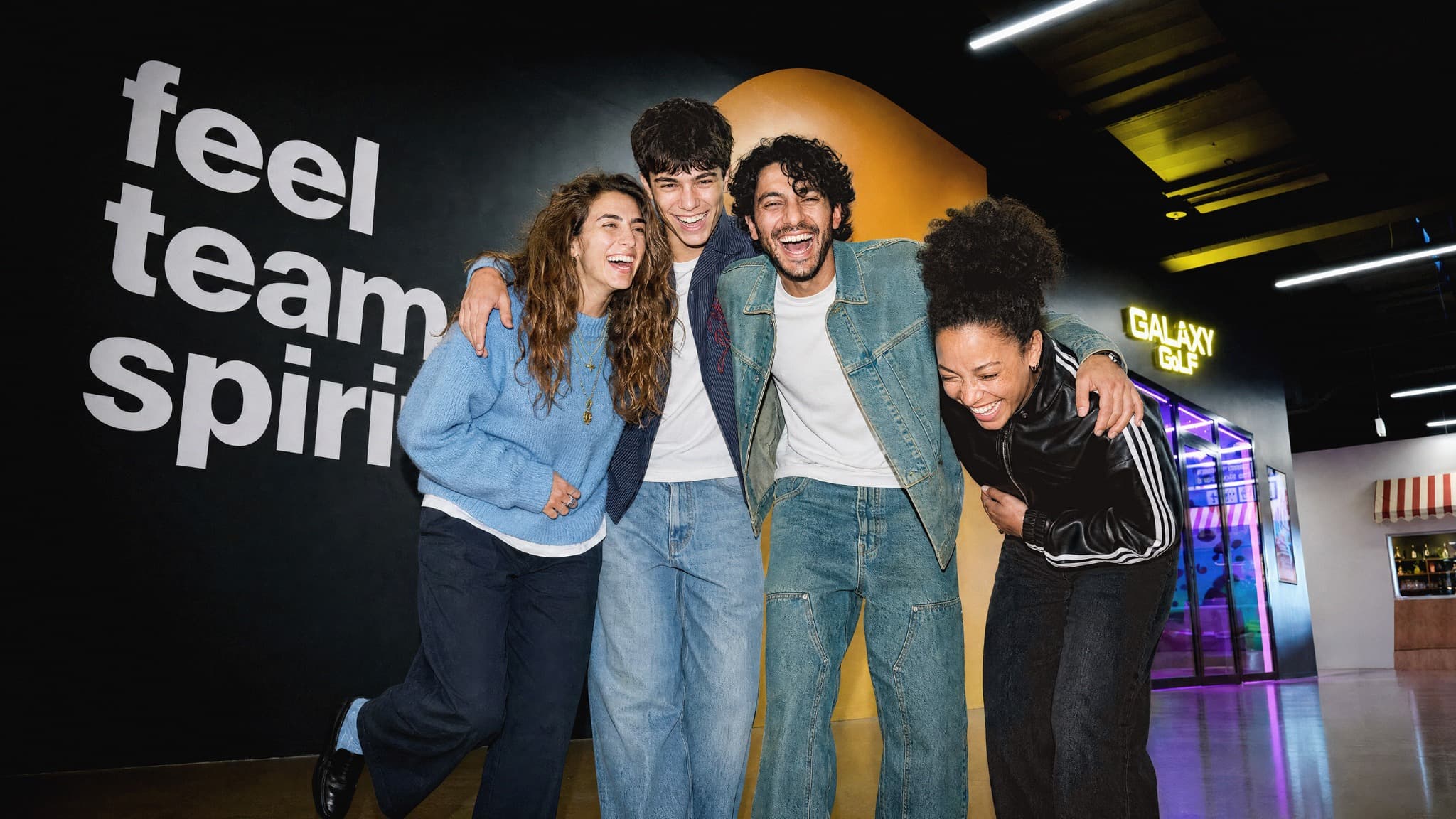 Vier Erwachsene stehen lachend beisammen vor der «feel team spirit»-Wand bei The Yards.