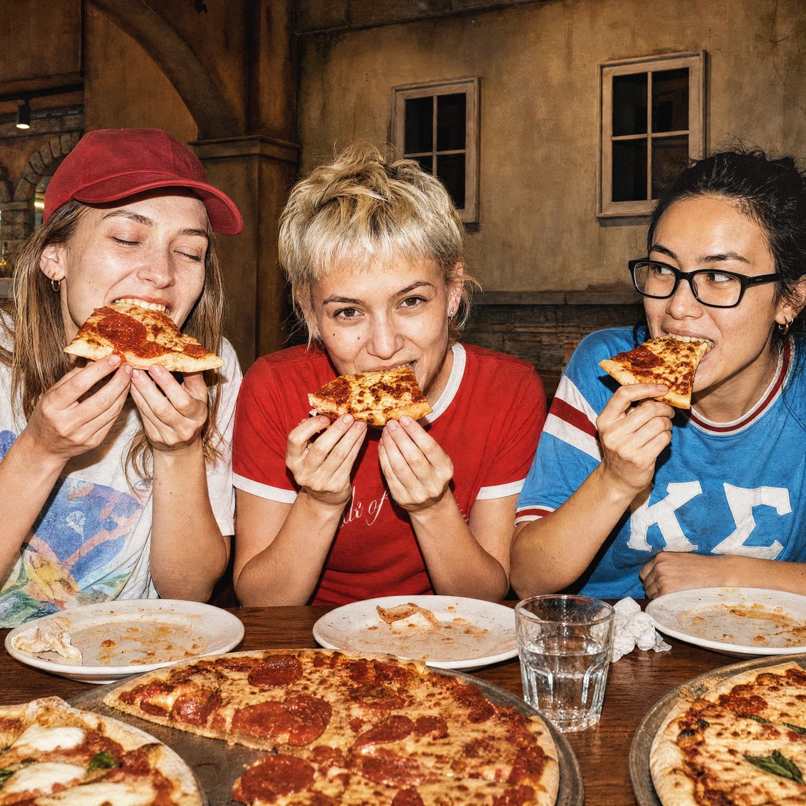 Drei junge Frauen essen gemeinsam Pizza am Tisch im Restaurant Piazza Meraviglia bei The Yards – ein Motiv für Treffen mit Freundinnen.