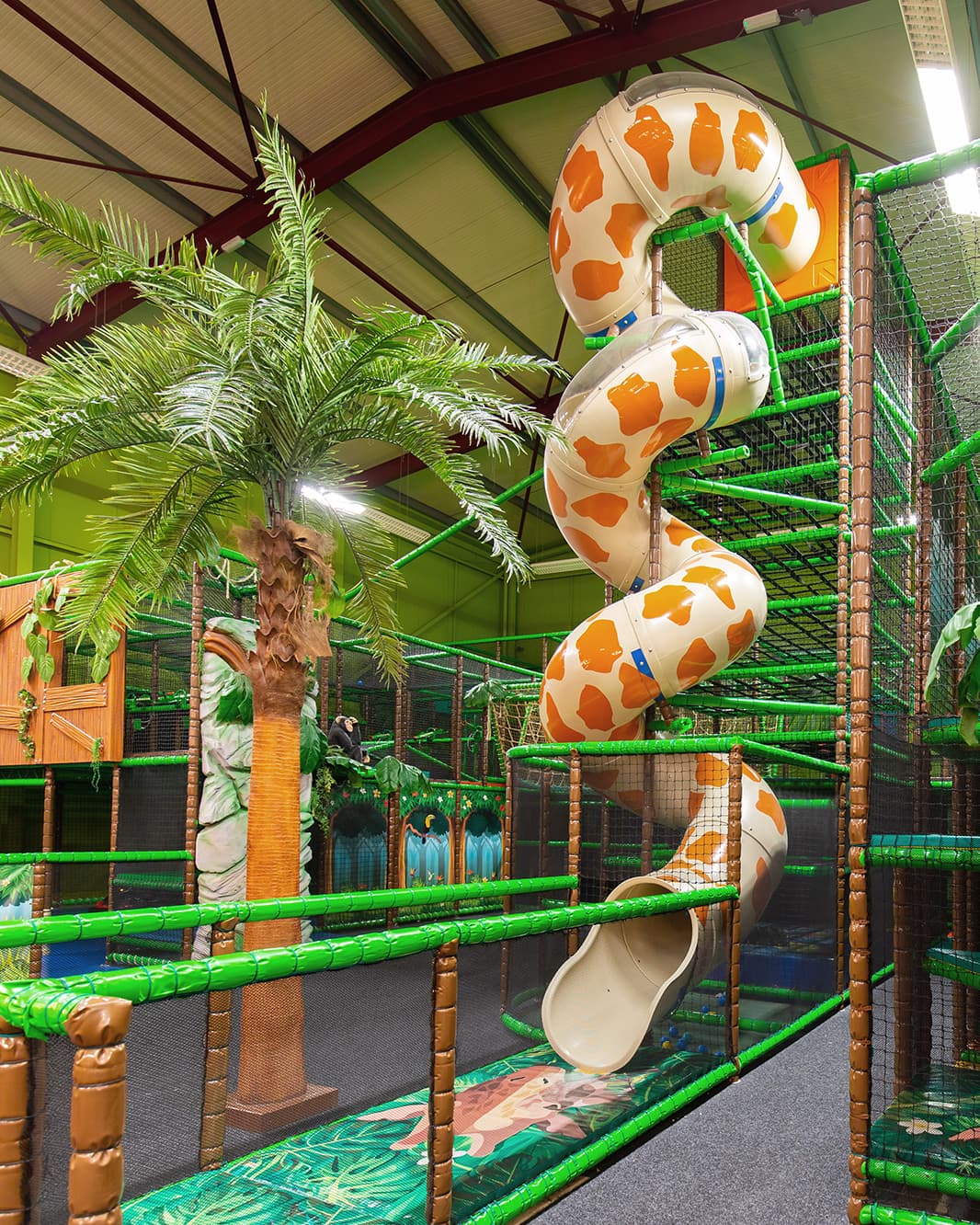Grosse gewundene Röhrenrutsche mit orangefarbenem Muster in der grünen Indoor-Kletterlandschaft von Monkey Town bei The Yards in Rümlang.