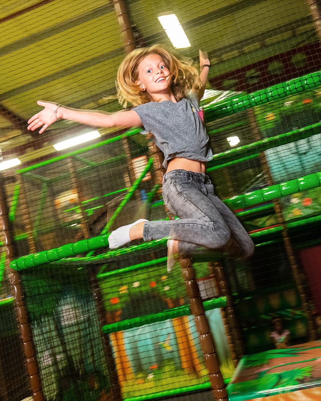 Lachendes Mädchen hüpft vor einem grünen Netz-Klettergerüst im Monkey Town bei The Yards in Rümlang.