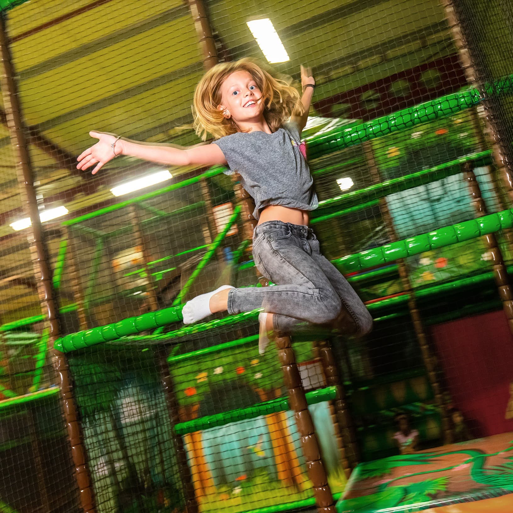 Mädchen springt mit ausgebreiteten Armen vor einem grünen Kletterparcours im Monkey Town bei The Yards in Rümlang.