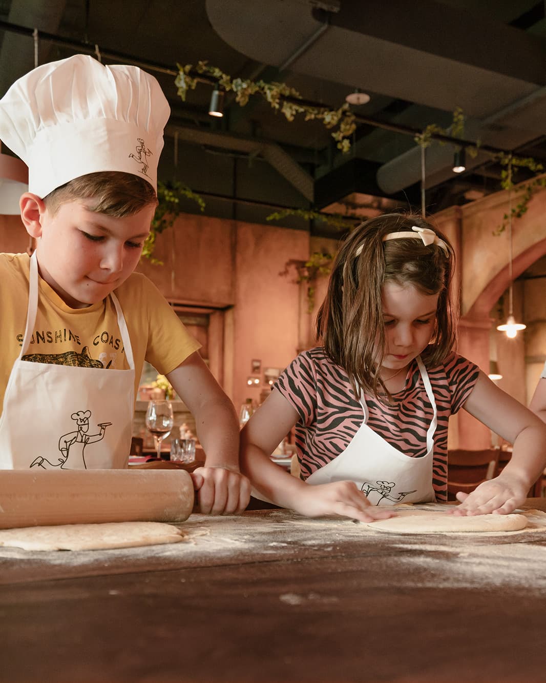 Zwei Kinder mit Kochschürzen rollen und formen Pizzateig beim Pizza-Workshop im Ristorante Piazza Meraviglia bei The Yards in Rümlang.