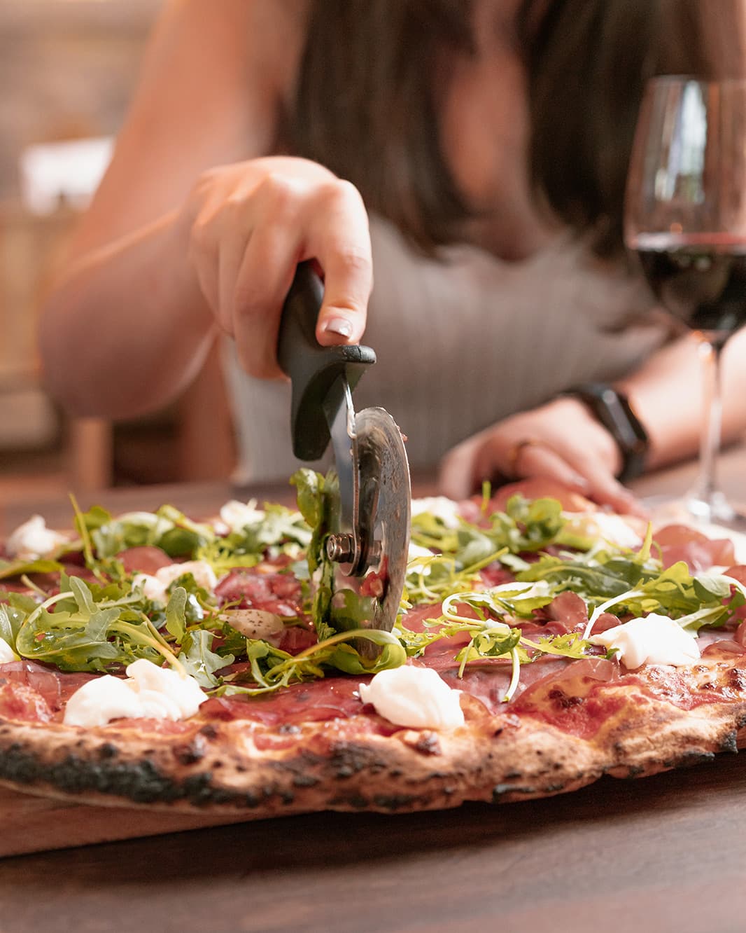 Eine Person schneidet eine knusprige Pizza mit Rucola und cremigem Käse im Ristorante Piazza Meraviglia bei The Yards in Rümlang.