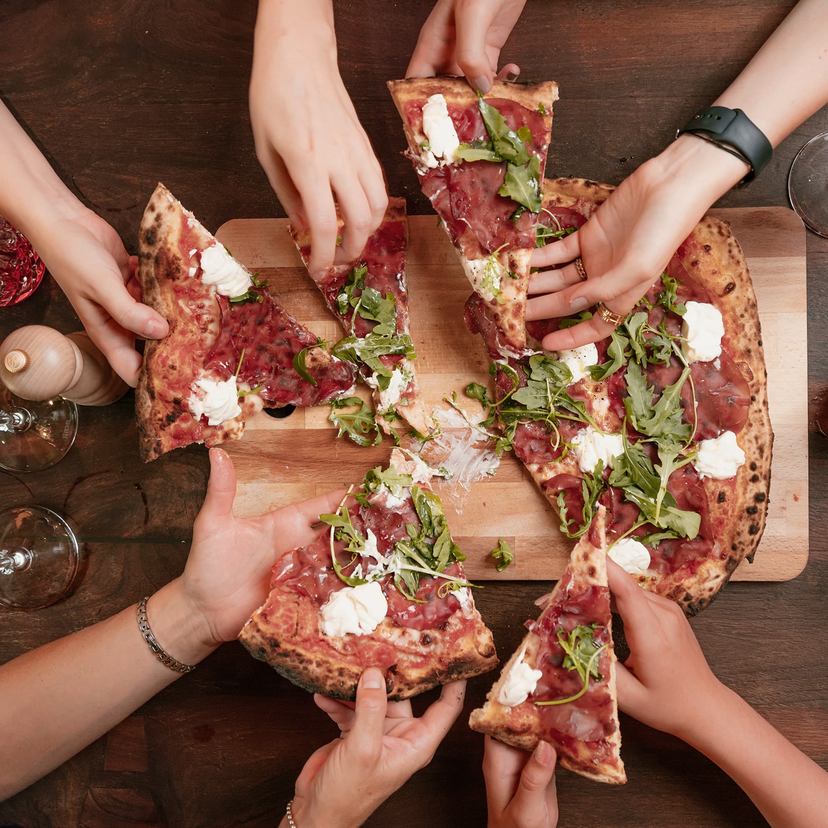 Mehrere Gäste nehmen sich gemeinsam Stücke einer frisch gebackenen Pizza im Ristorante Piazza Meraviglia bei The Yards in Rümlang.