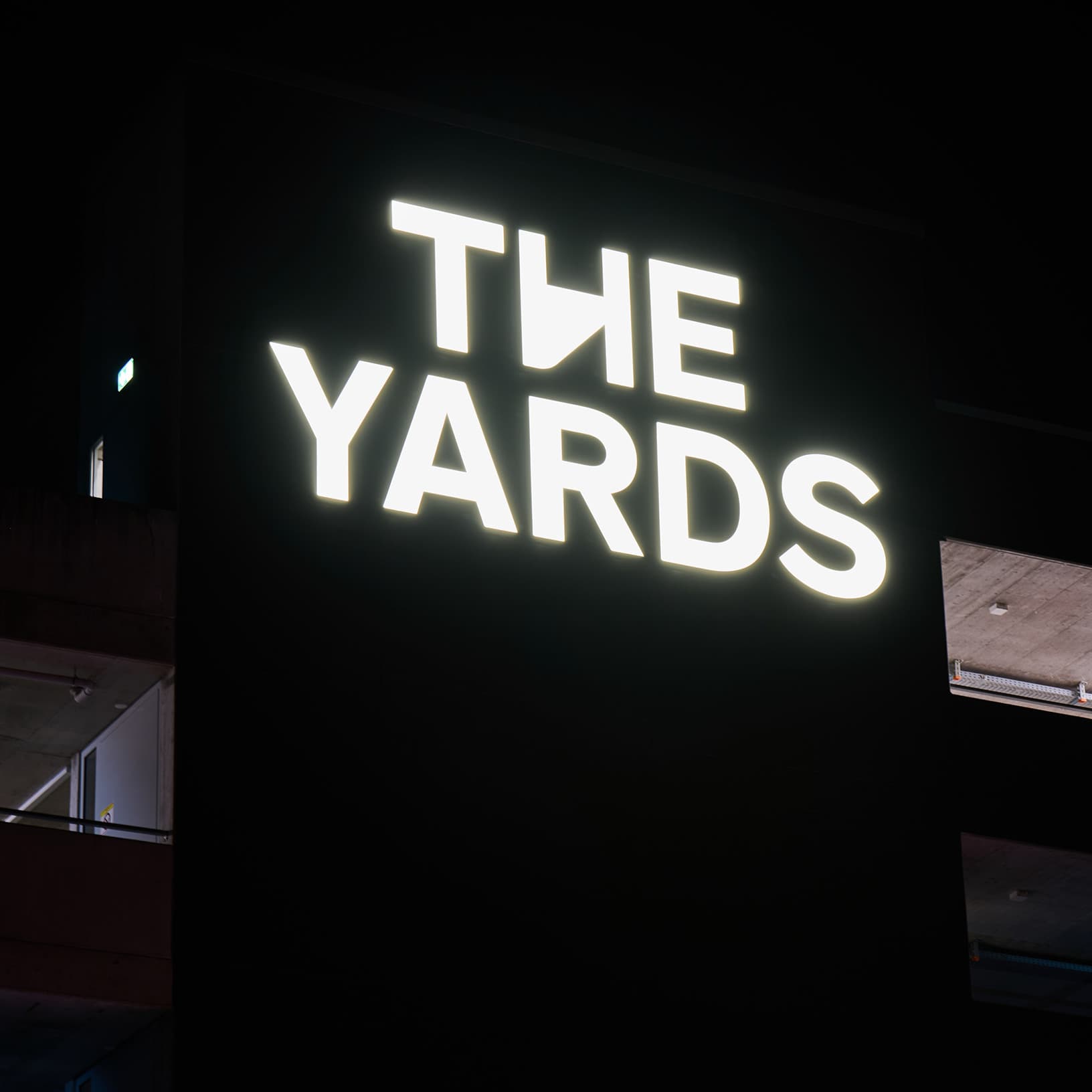 Das weiss leuchtende The Yards Logo an der dunklen Aussenfassade des Centers in Rümlang bei Nacht.