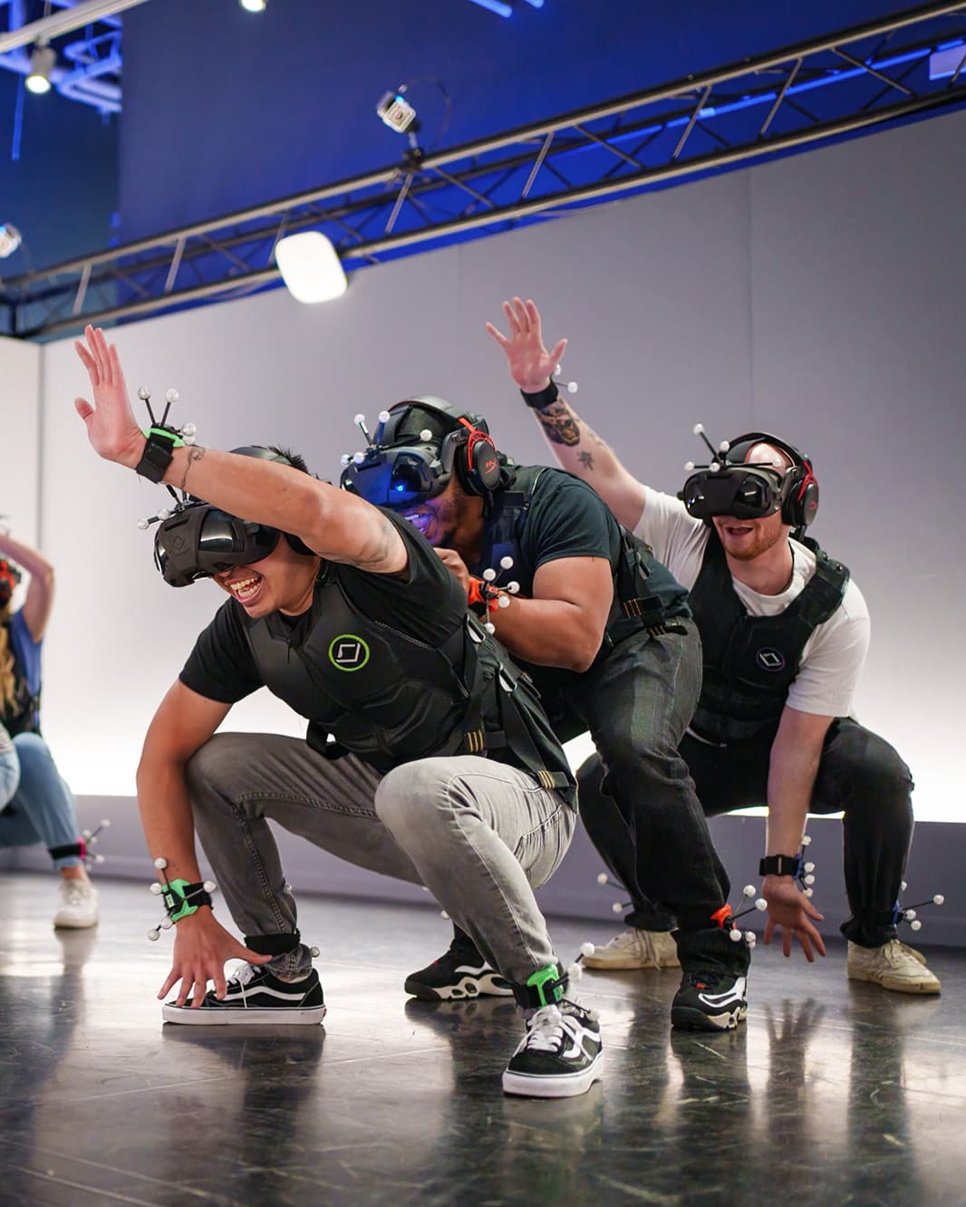 Drei Spieler mit VR-Brillen und Motion-Tracking-Ausrüstung gehen in die Hocke und strecken ihre Arme aus.
