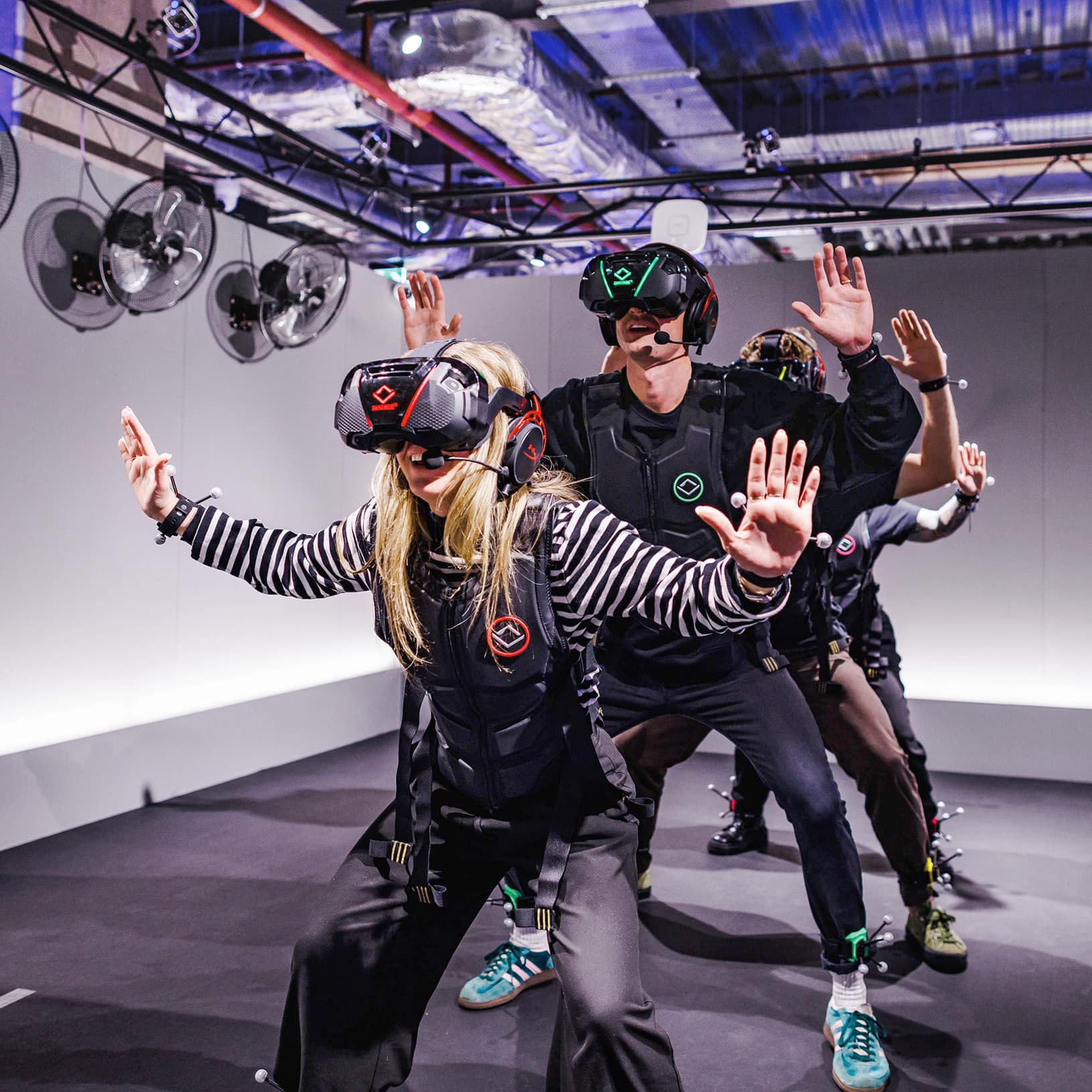 Gruppe mit VR-Brillen und Motion-Tracking-Ausrüstung erlebt gemeinsam ein virtuelles Abenteuer bei Sandbox VR.