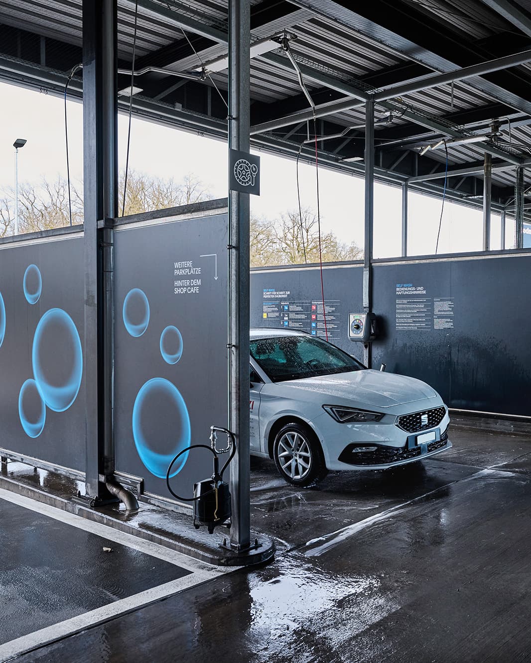 Weisses Auto in einer Self-Wash-Waschbox mit Waschlanze und Bedienungshinweisen bei The Yards in Rümlang.