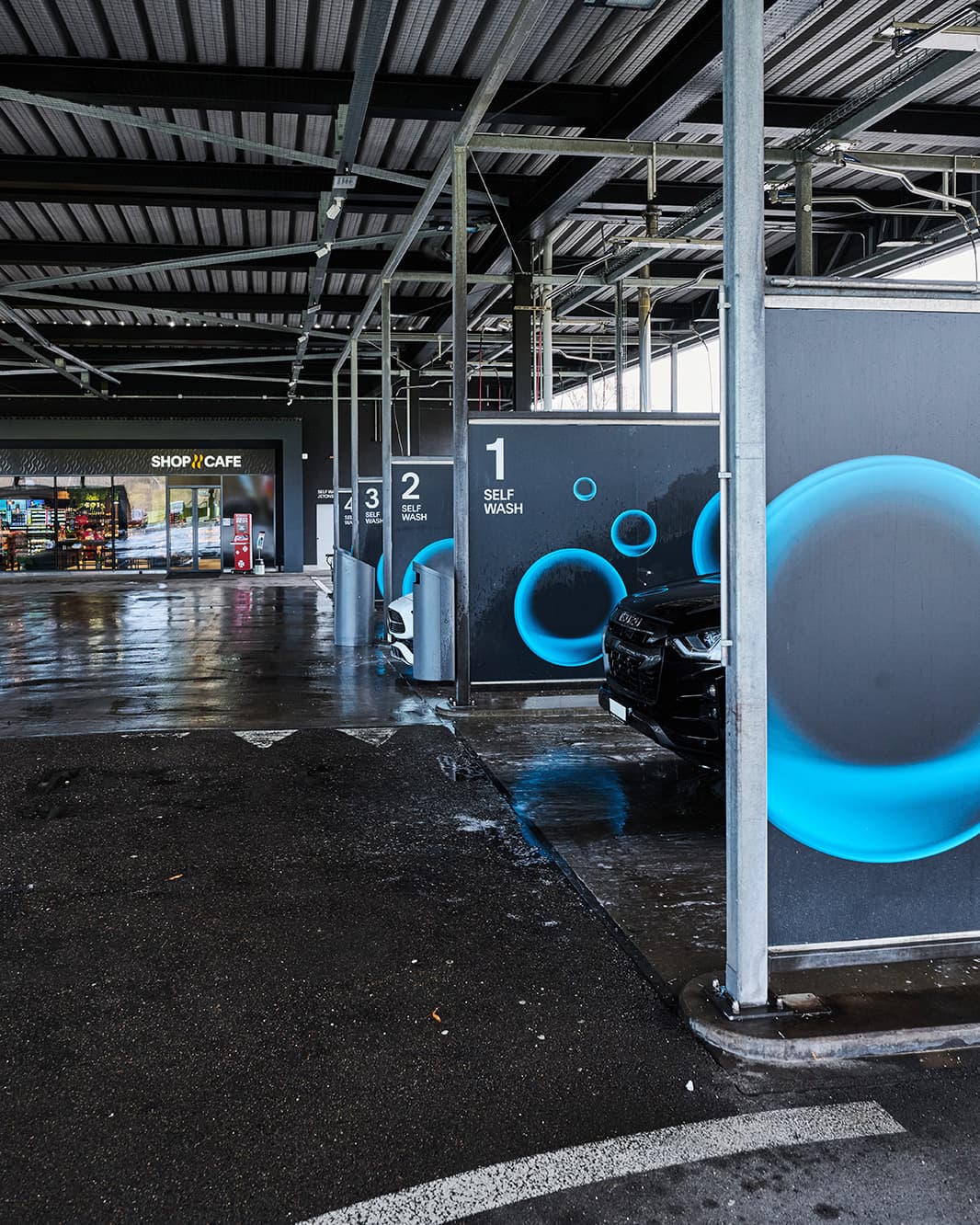 Blick entlang der überdachten Self-Wash-Waschboxen in Richtung Shop & Café bei The Yards in Rümlang.