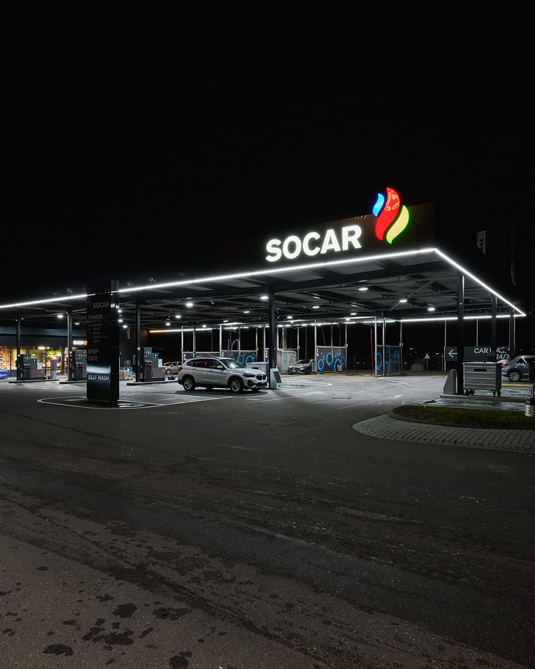 Weitwinkelansicht der SOCAR Tankstelle bei The Yards in Rümlang mit beleuchtetem Dach und Zufahrt.