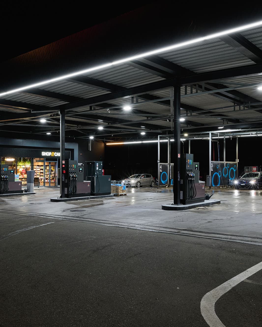 Zapfsäulen und der beleuchtete SOCAR Shop & Café unter dem Tankstellendach bei The Yards in Rümlang.